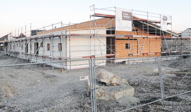 Rohbau der neuen Kindertagesstätte Schwalbennest in Schnelldorf während der Bauphase. Das eingeschossige Gebäude in Holzbauweise ist eingerüstet und teilweise mit Fassadenplatten verkleidet. Am Baugerüst sind Banner von Bauer Holzbau angebracht.