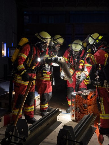 Mehrere Feuerwehrleute mit Atemschutz arbeiten während der gemeinsamen Übung in einer Fertigungshalle von Bauer Holzbau mit Schläuchen und Einsatzgeräten.