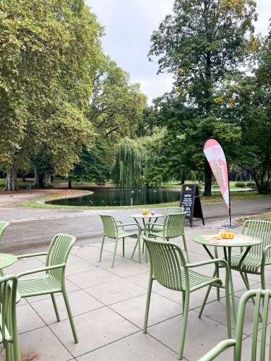 Grüne Tische und Stühle auf der Terrasse des neuen Kiosks KÖSK mit Blick auf den Teich und die umliegenden Bäume im Unteren Schlossgarten Stuttgart.