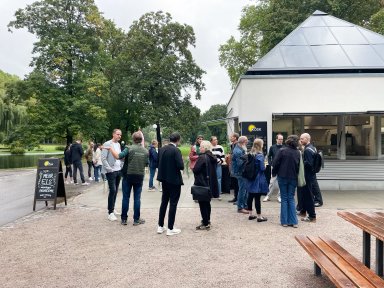 Besucher und Projektbeteiligte unterhalten sich bei der Eröffnung des neuen Kiosks KÖSK in Stuttgart. Im Hintergrund ist der Holzbau mit seinen markanten Pyramidendächern zu sehen.