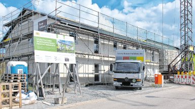 Neubau des zweiten städtischen Mehrfamilienhauses im Wohngebiet Röschenhof in Feuchtwangen. Das Gebäude in Holzständerbauweise ist eingerüstet und befindet sich nach der Montage der vorgefertigten Holzelemente im weiteren Ausbau. Vor der Baustelle steht ein Lkw von Bauer Holzbau.