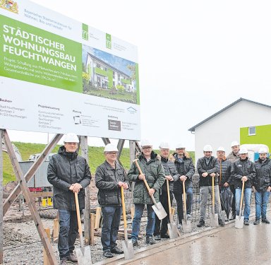 Vertreter der Stadt Feuchtwangen, der Projektplanung und der ausführenden Baufirma Bauer Holzbau beim symbolischen Spatenstich für das zweite städtische Mehrfamilienhaus im Wohngebiet Röschenhof. Die Beteiligten stehen mit Spaten vor der Bautafel für den Neubau mit sechs Mietwohnungen.