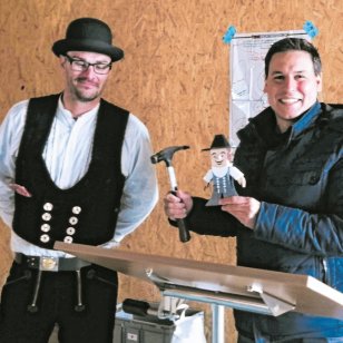 Zimmermann Achim Dausch von Bauer Holzbau überreicht Schnelldorfs Bürgermeister Tobias Strauß beim Richtfest der neuen Kindertagesstätte Schwalbennest einen Hammer und eine kleine Zimmermannsfigur. Im Hintergrund ist die Holzkonstruktion des Neubaus zu sehen.