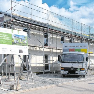 Neubau des zweiten städtischen Mehrfamilienhauses im Wohngebiet Röschenhof in Feuchtwangen. Das Gebäude in Holzständerbauweise ist eingerüstet und befindet sich nach der Montage der vorgefertigten Holzelemente im weiteren Ausbau. Vor der Baustelle steht ein Lkw von Bauer Holzbau.