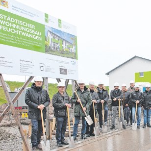 Vertreter der Stadt Feuchtwangen, der Projektplanung und der ausführenden Baufirma Bauer Holzbau beim symbolischen Spatenstich für das zweite städtische Mehrfamilienhaus im Wohngebiet Röschenhof. Die Beteiligten stehen mit Spaten vor der Bautafel für den Neubau mit sechs Mietwohnungen.